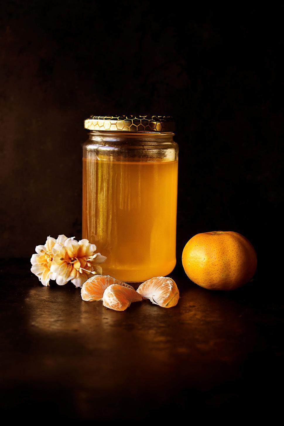 Free Image of Jar of honey with orange and flower on dark background 