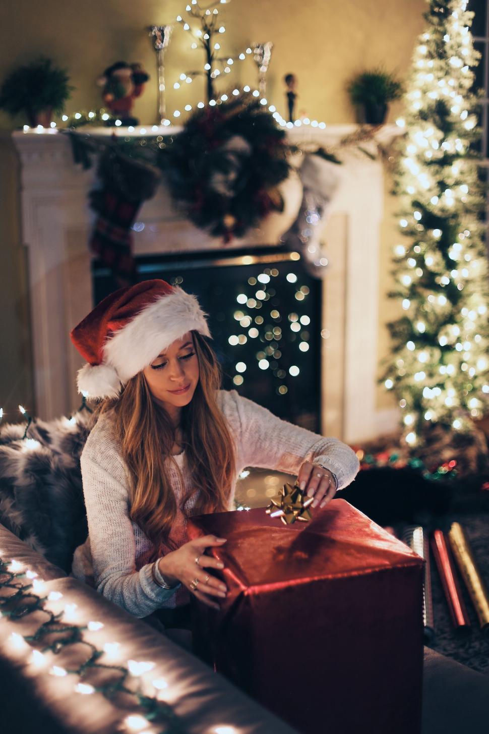 Free Image of Woman in Santa hat wrapping a Christmas present warmly. 