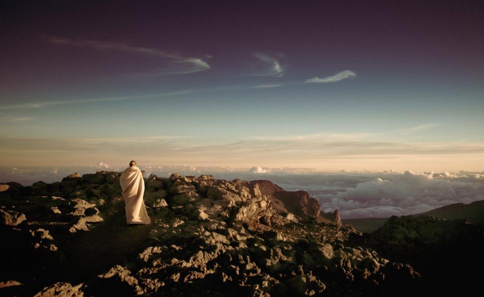 Free Image of Figure wrapped in blanket stands on rocky mountain peak 