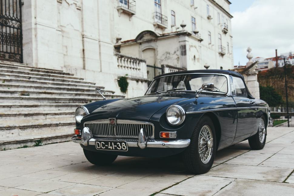 Free Image of Vintage black convertible car parked outside a historic building 