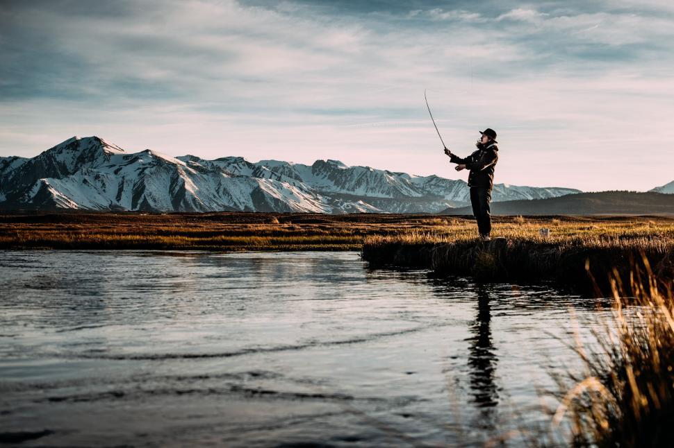 Free Image of Person fly fishing in a river with snow-capped mountains. 