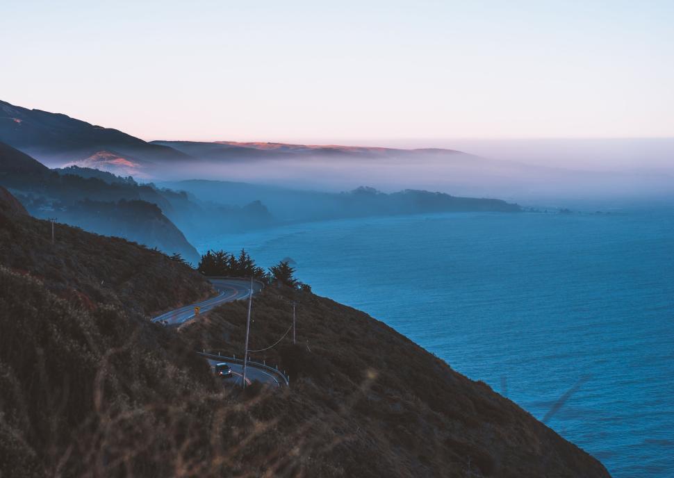 Free Image of Scenic coastal road with foggy hills at dawn 