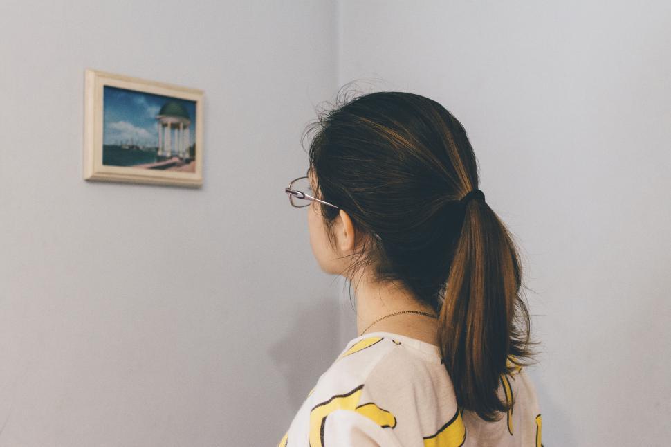 Free Image of Woman looking at framed seaside picture on a wall 