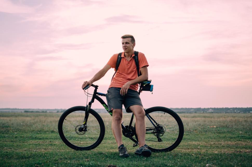 Free Image of Man in orange shirt and backpack resting on bicycle outdoors. 