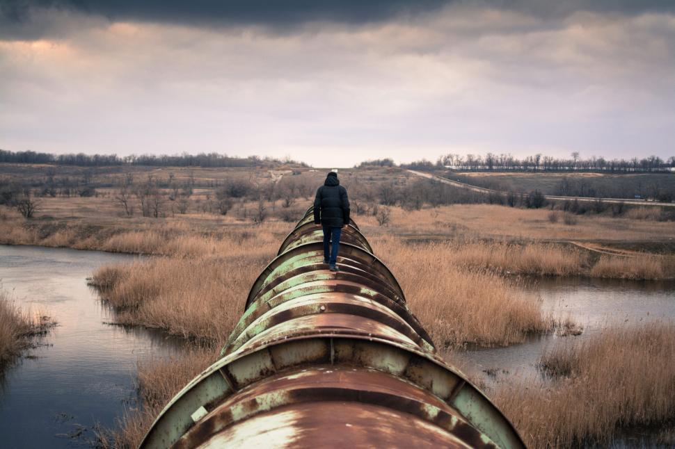 Free Image of Man walking on large rusted pipe in barren landscape 