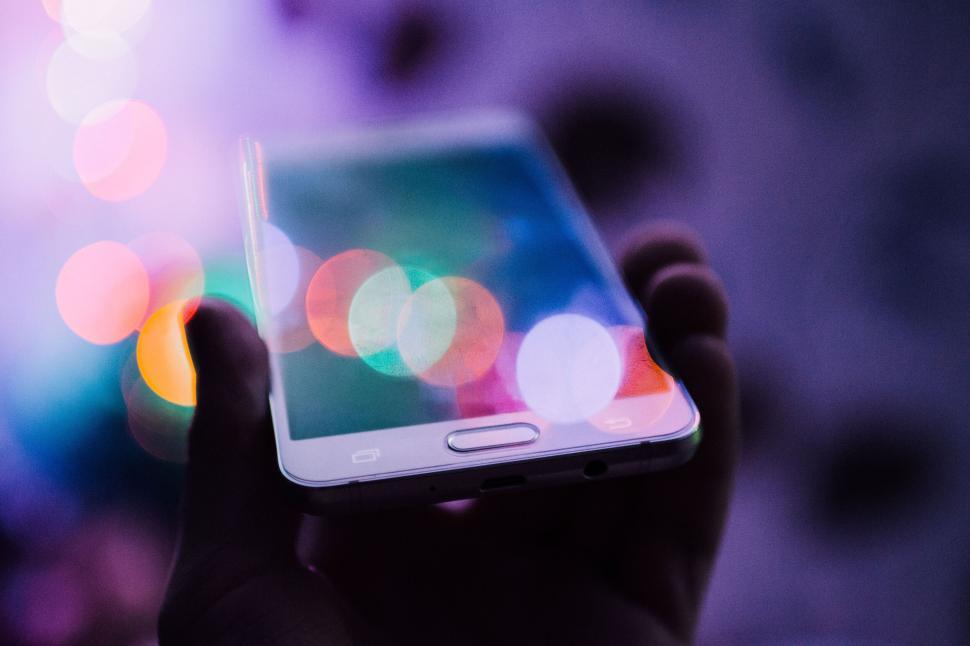 Free Image of Hand holding smartphone with colorful, out-of-focus lights 