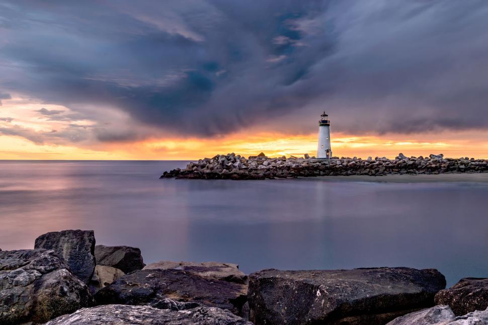 Free Image of Lighthouse at sunset under dramatic cloudy sky. 