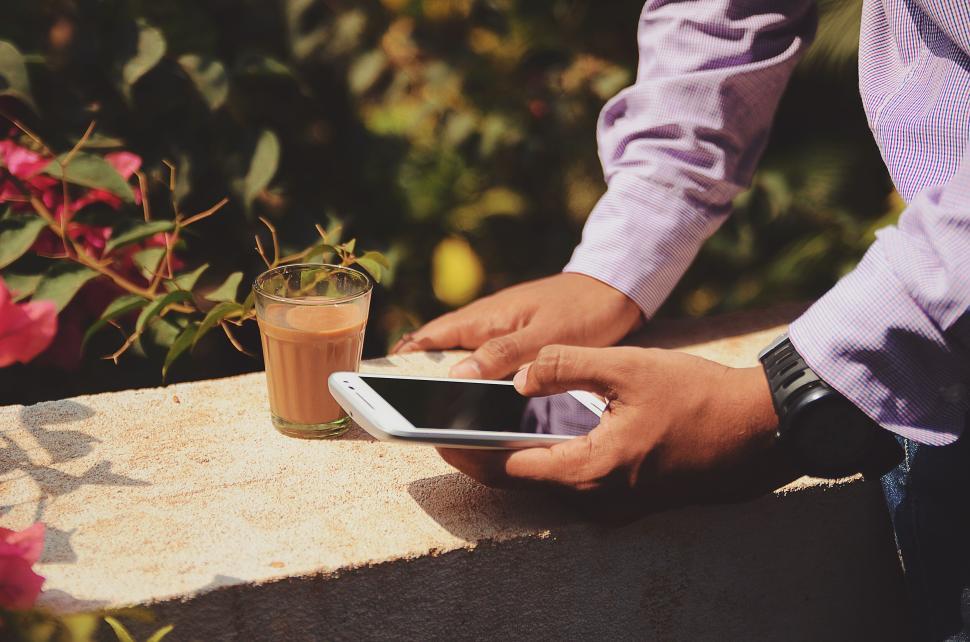Free Image of Man holding smartphone with coffee cup on the ledge. 
