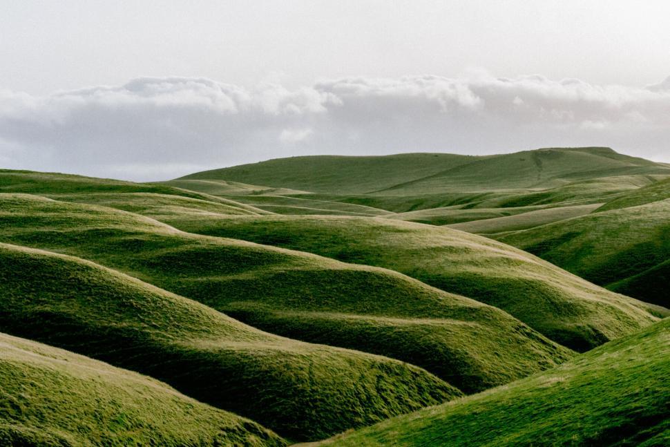 Free Image of Green rolling hills landscape under a cloudy sky 