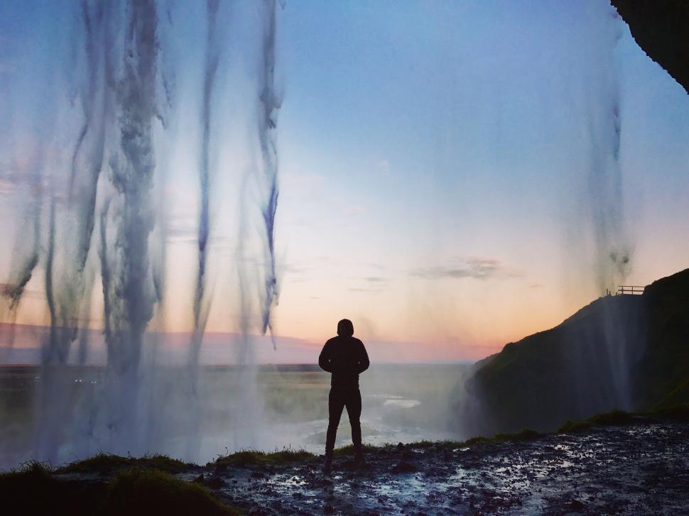 Free Image of Person standing behind a majestic waterfall at sunset. 