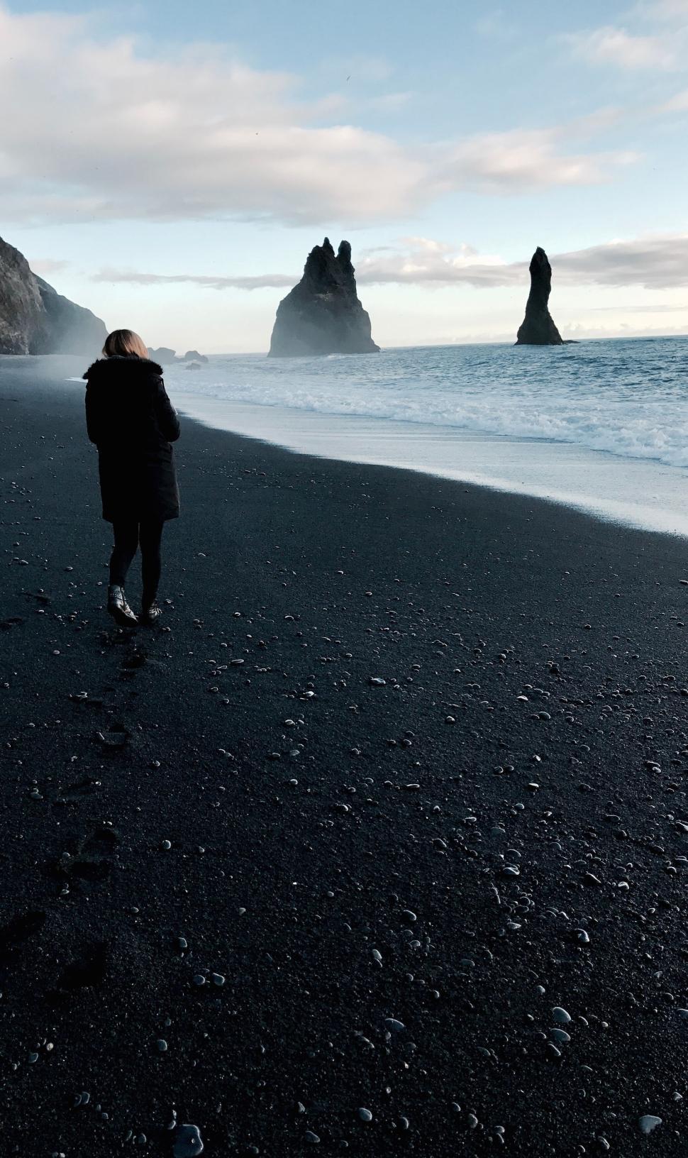 Free Image of Person walking on black sand beach with big rock formations. 
