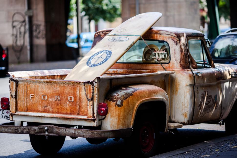 Free Image of Rusty vintage Ford truck with surfboard in urban setting. 