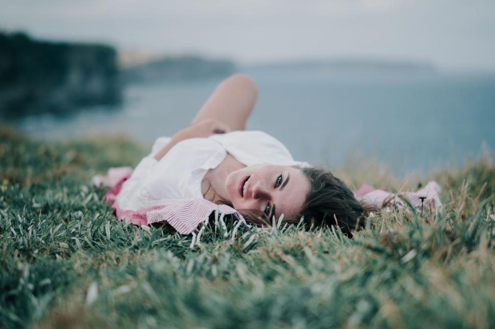 Free Image of Person resting on grassy cliff with ocean view. 