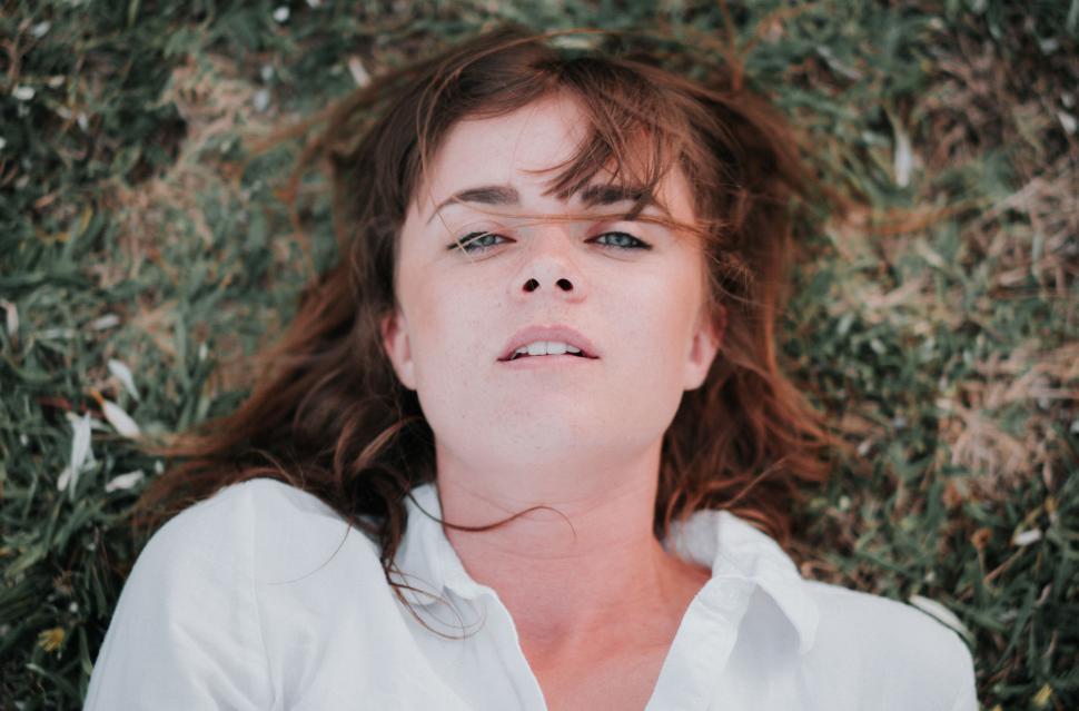 Free Image of Woman laying down on grass with relaxed expression. 
