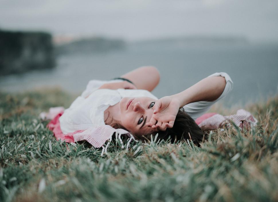 Free Image of Person lying on blanket in grassy field near water. 
