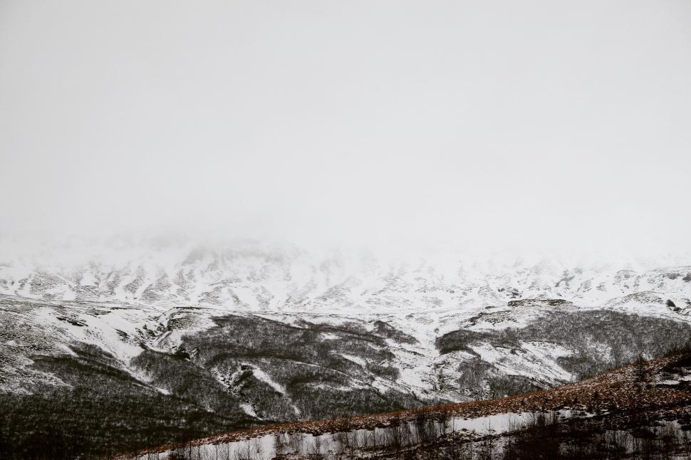 Free Image of Snow-covered landscape with fog-enshrouded mountains. 