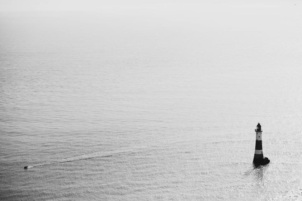 Free Image of Solitary lighthouse in calm sea with small boat nearby. 