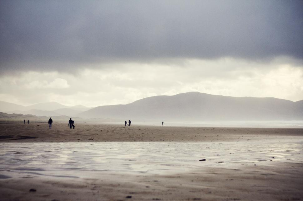 Free Image of Wide sandy beach with distant figures beneath cloudy sky 