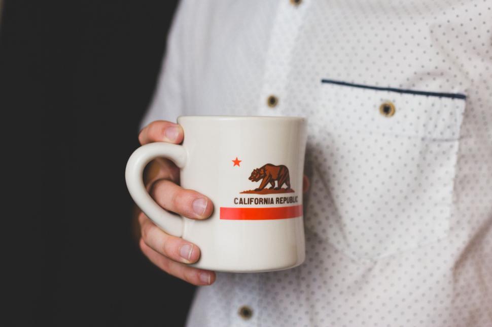 Free Image of Hand holding a California Republic mug in white shirt. 