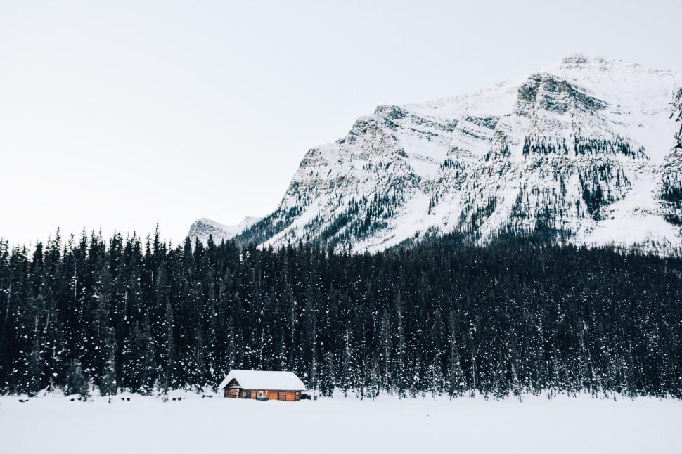 Free Image of Snow-covered cabin nestled within pine forest and mountains. 