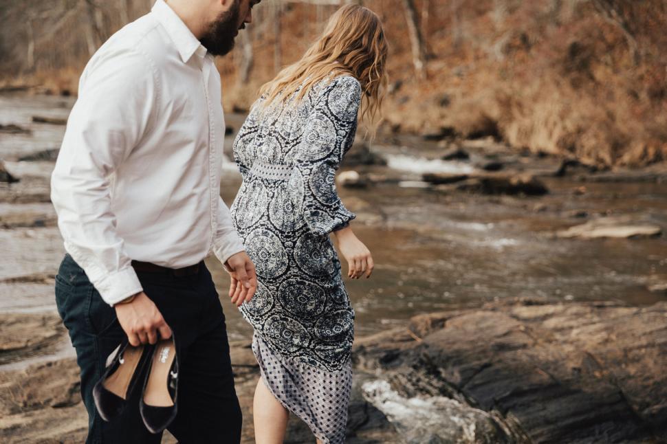 Free Image of Couple walking near river in nature, holding shoes. 