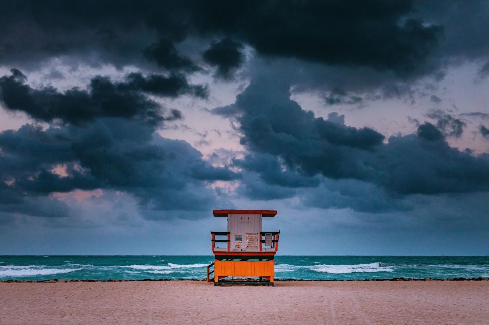 Free Image of Lifeguard hut under dramatic sky by the ocean shore. 
