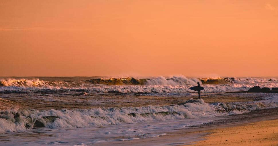 Free Image of Surfer with surfboard gazing at waves during sunset. 
