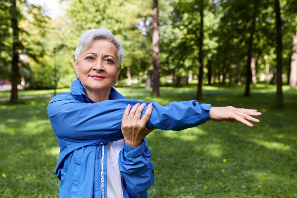 Free Image of Summertime image of healthy active retired woman smiling, stretching arm muscles after running training outdoors, posing in forest. Health, well being, age, people, sports and activity concept 
