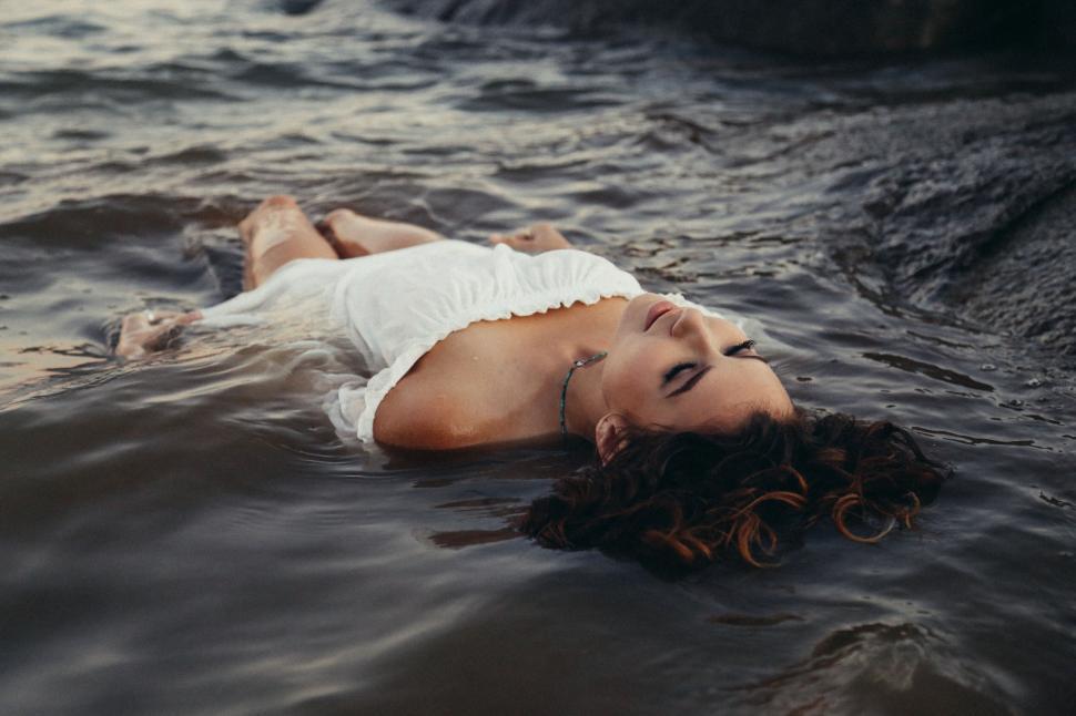 Free Image of Person in white dress lying down in water and rocks 