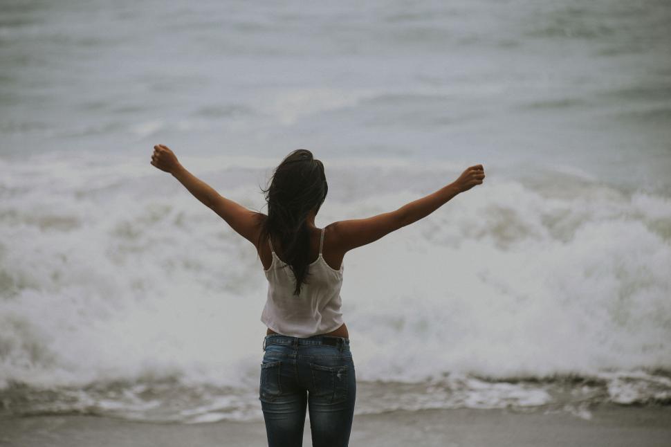 Free Image of Woman standing on the beach with arms open wide 