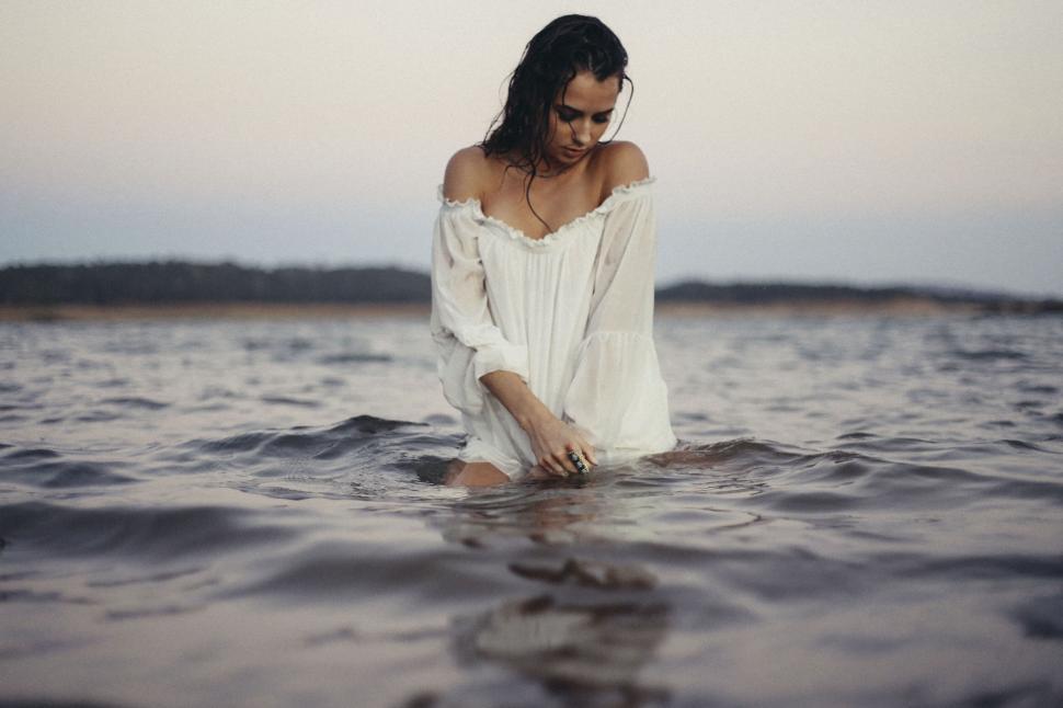 Free Image of Woman in white dress standing in the water at dusk 