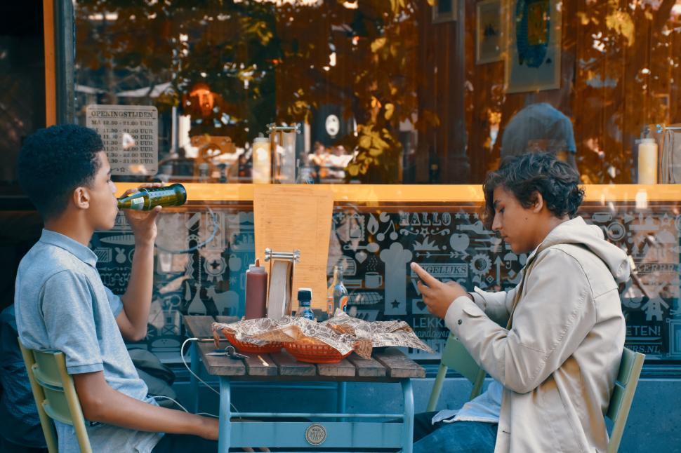 Free Image of Two friends relaxing outside a cafe with drinks and food 