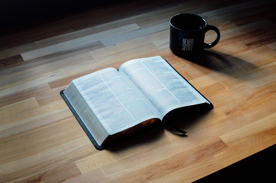 Free Image of Open book and mug on a wooden table with sunlight. 
