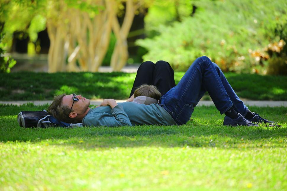 Free Image of Two people relaxing on green grass in a sunny park. 
