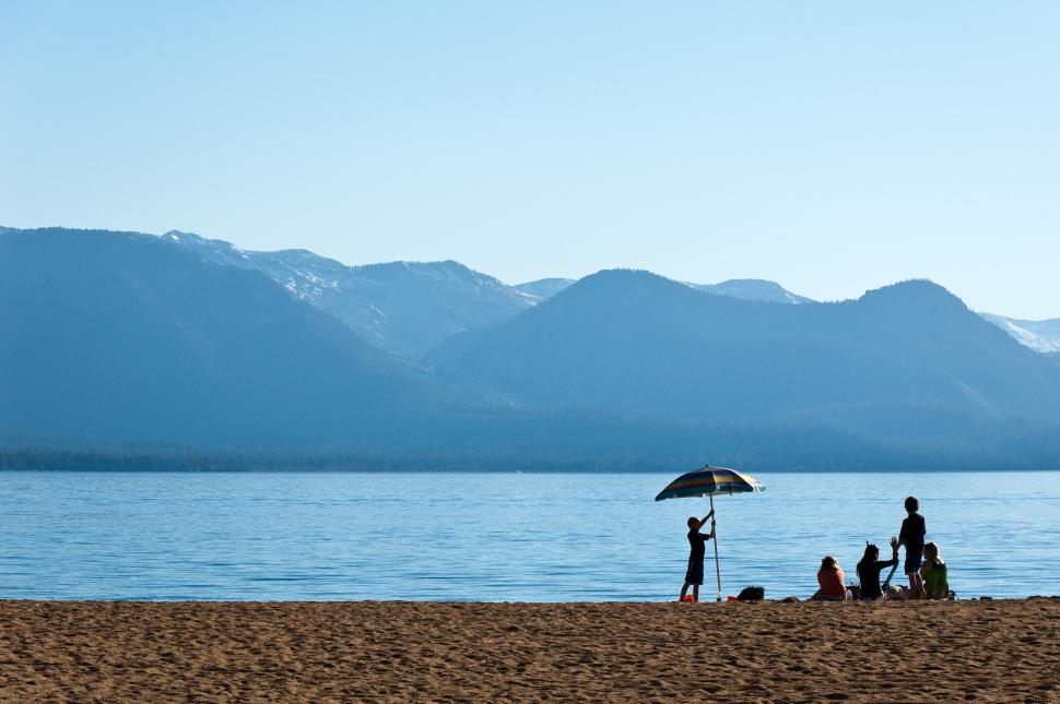 Free Image of Beach scene with people, umbrellas, and scenic mountains. 