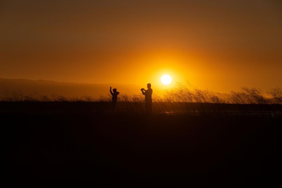 Free Image of Silhouetted figures pose with camera in sunset field. 