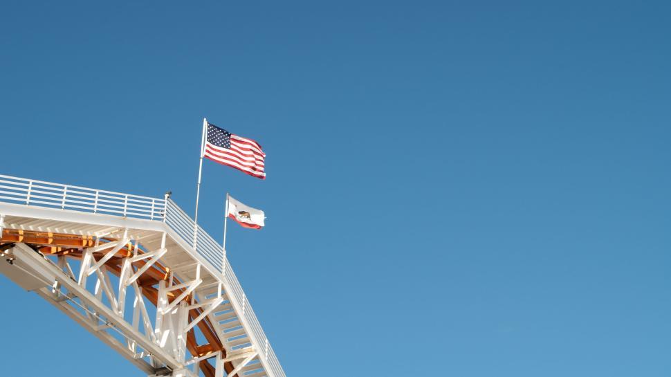 Free Image of Flags waving on a bridge against a clear blue sky 