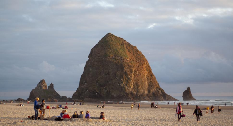 Free Image of People enjoying the beach near a large sea stack 