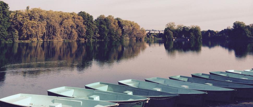 Free Image of Row of boats on a calm lake with scenic backdrop. 