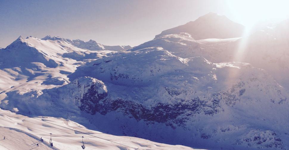 Free Image of Snow-covered mountains under clear sky with bright sun. 