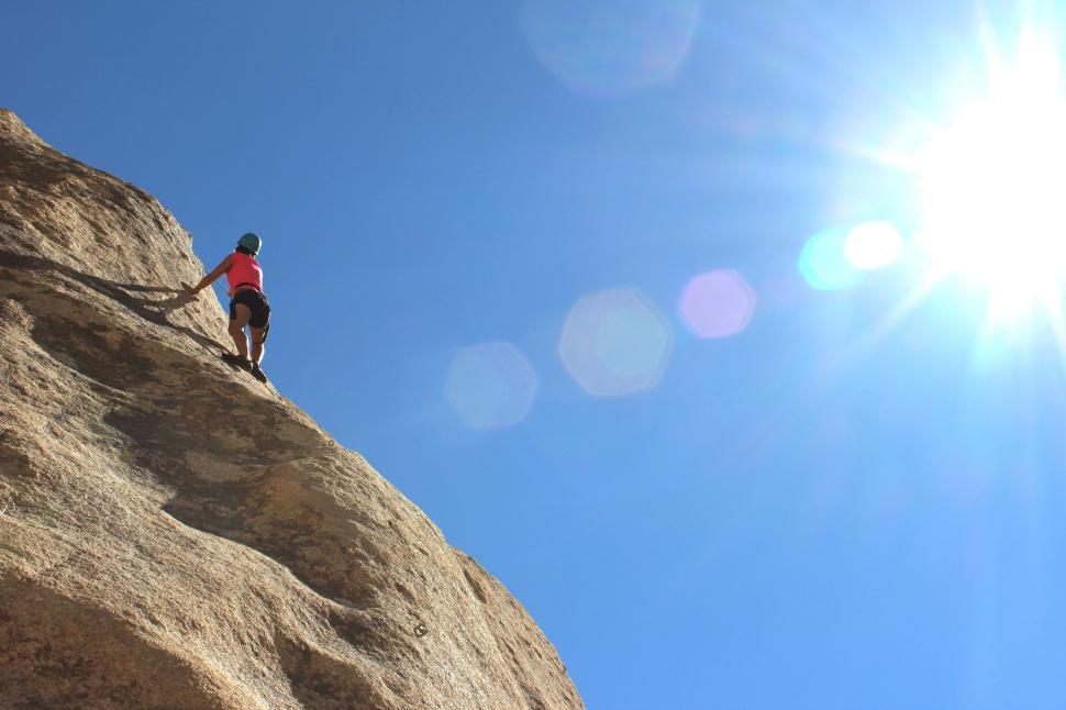 Free Image of Climber scaling a rock wall against a sunny blue sky. 