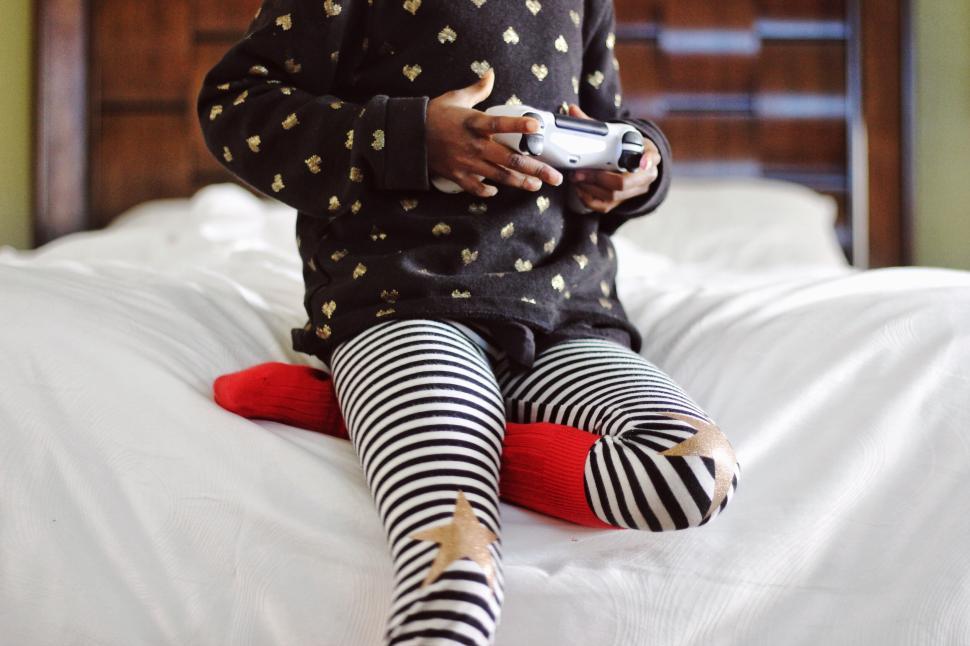 Free Image of Child with game controller in bed wearing striped pants. 