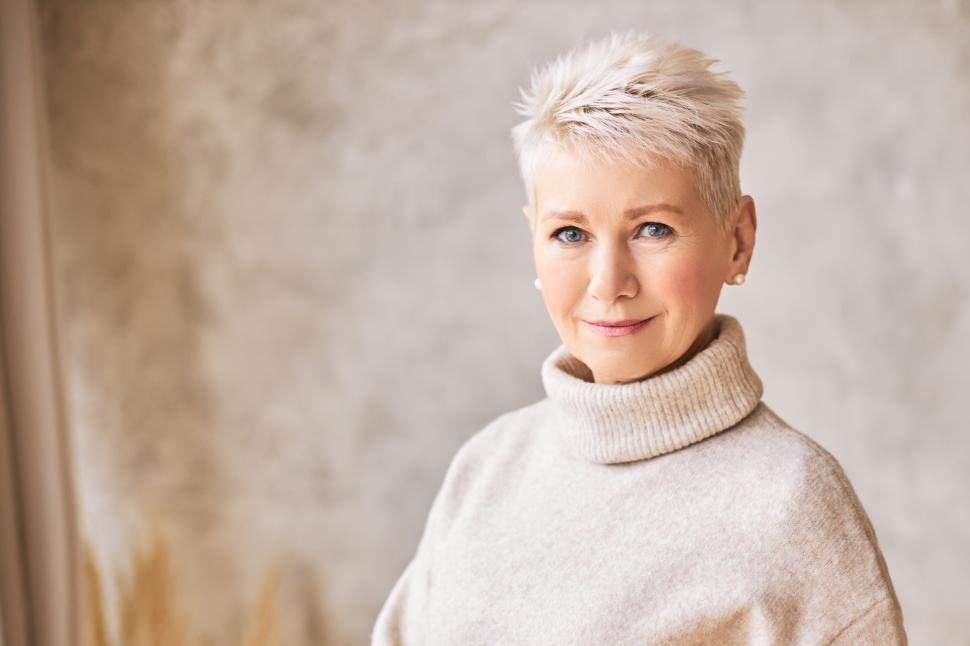 Free Image of Horizontal shot of blonde fifty year old European female with stylish pixie haircut and blue eyes smiling at camera, having confident look posing isolated indoors. Aged people and maturity concept 