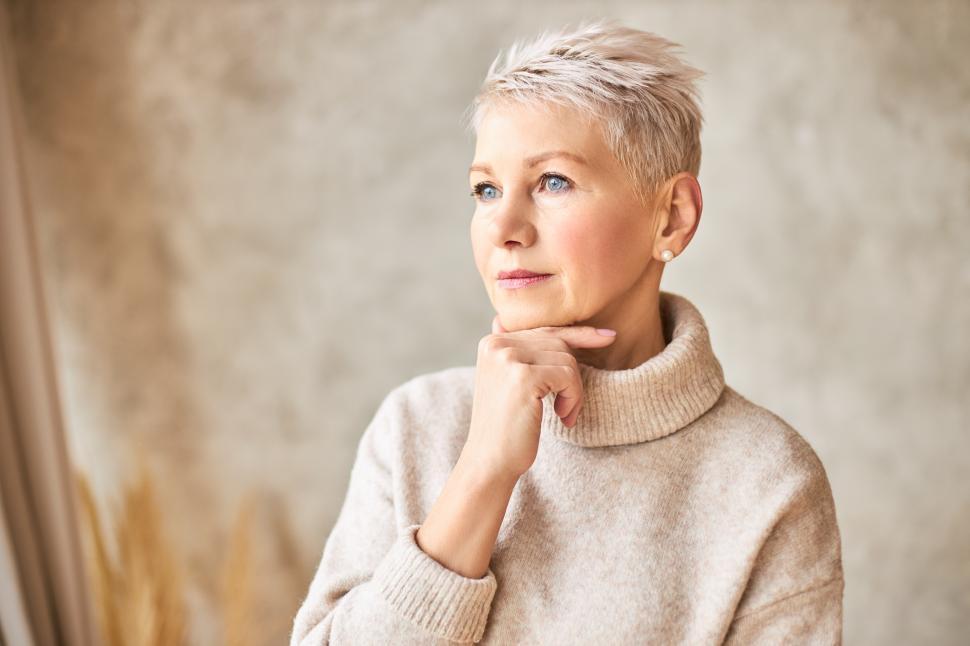 Free Image of Aging, beauty, style, elegance and fashion concept. Portrait of thoughtful middle aged lady wearing beige turtleneck sweater with hand under chin, pondering, having worried facial expression 