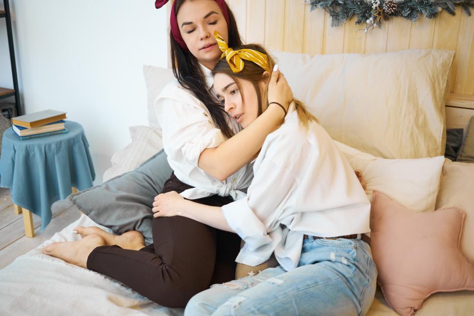 Free Image of Young female sitting on bed trying to support her best friend in trouble, telling words of consolation and encouragement. Teenage girl weeping on lap of sister who is comforting her in despair 