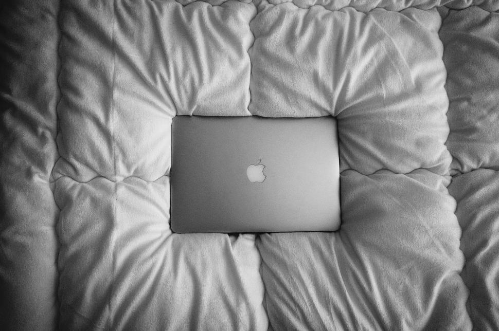 Free Image of Closed laptop lying on white comforter on a bed 