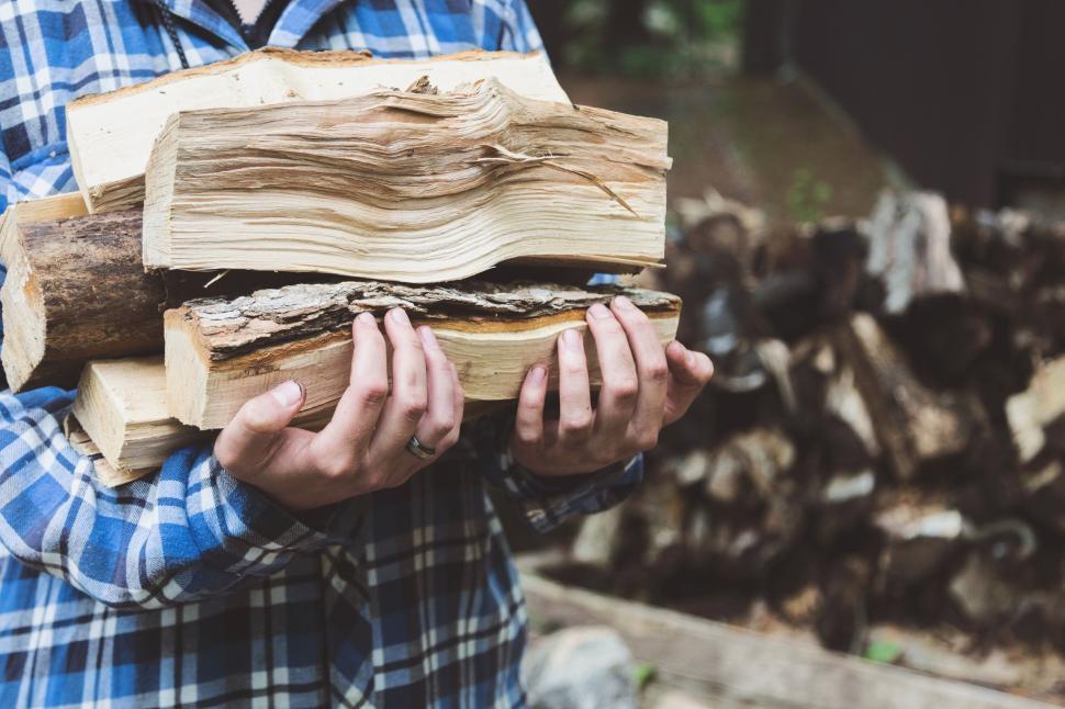 Free Image of Person holding firewood in a plaid shirt outdoors 