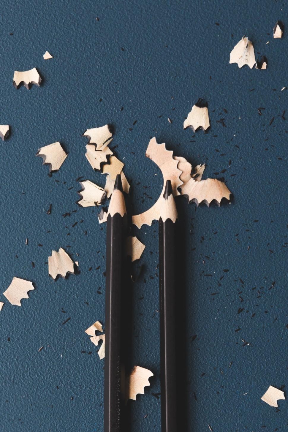 Free Image of Two sharpened black pencils with shavings on blue table 