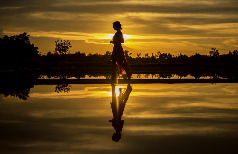 Free Image of Silhouette of a woman walking by a reflective water body. 