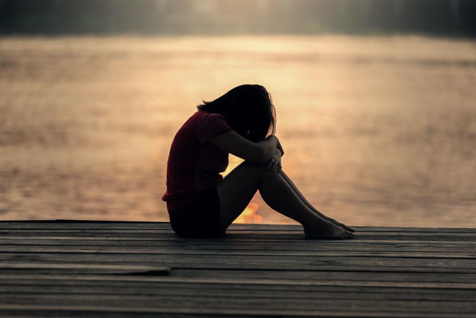 Free Image of A person sitting alone on a wooden dock at sunset. 